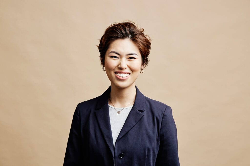 Studio headshot by Photoform* of woman smiling wearing a blue jacket against cream background.