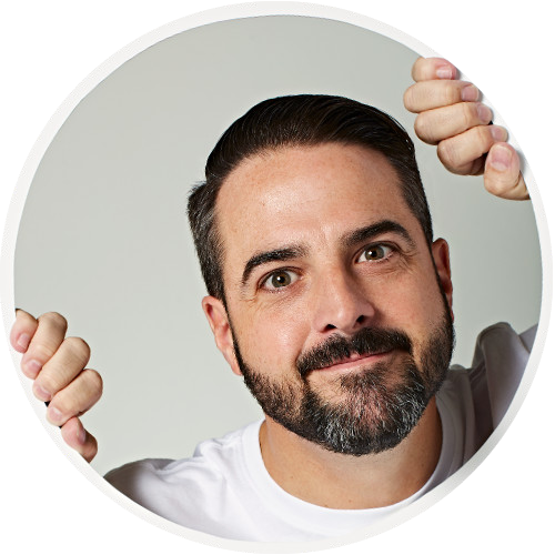 Creative LinkedIn profile picture of Chris Hincey.
Chris is peering through a mockup of a circle with his hands resting against the circle.
He's wearing a white tshirt.