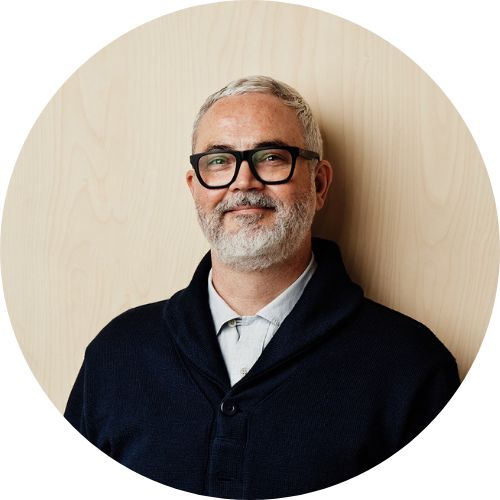 A LinkedIn profile picture for an architect.
Will is photographed against a plywood background.
He's wearing a navy coat and buttoned up shirt.