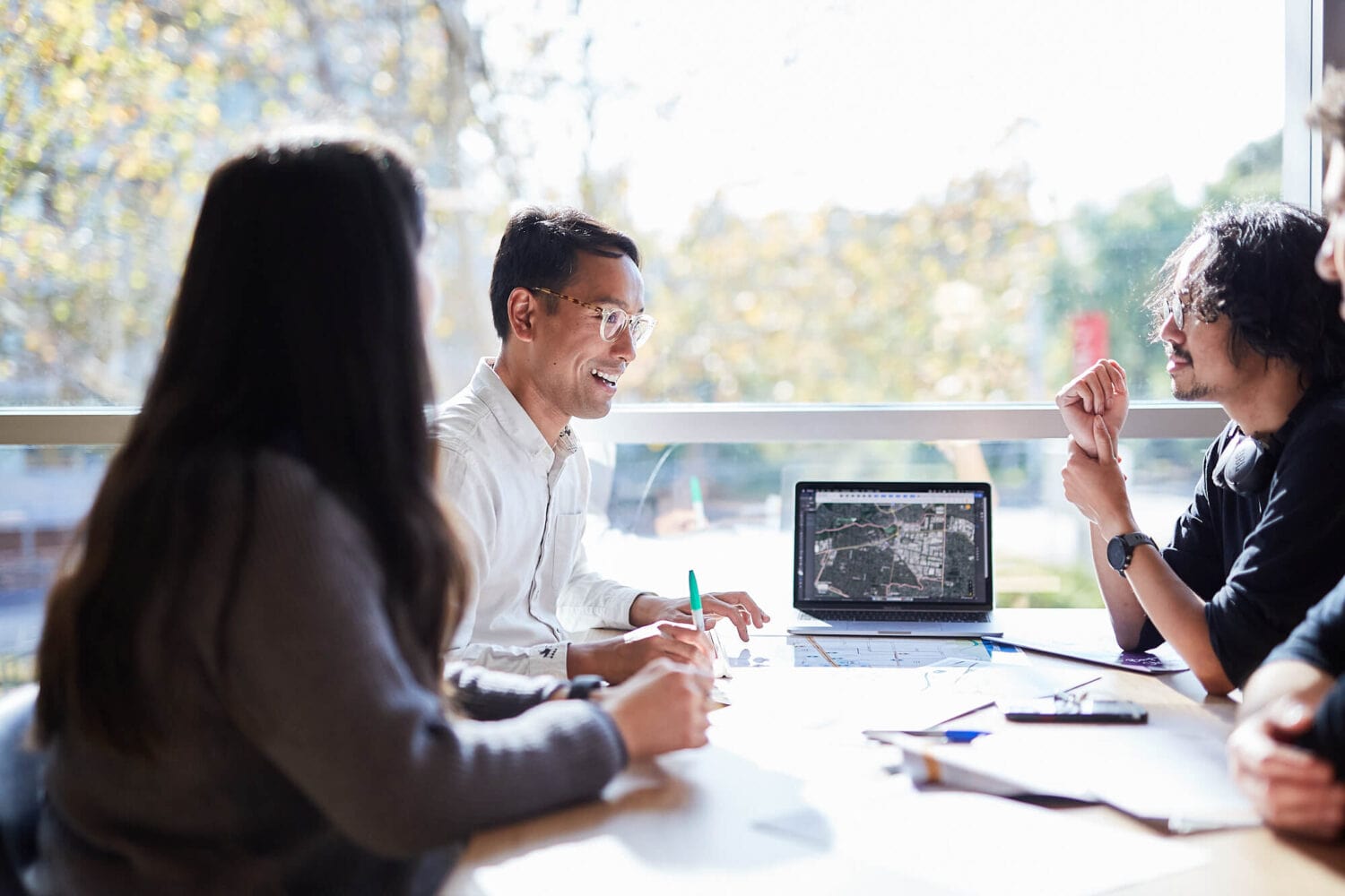Example of custom business photography by Photoform* for client CoFutures.
CoFutures are in a meeting in front of a large window looking out over some trees and a road.
There's a laptop on the table with a map on the screen.
One man is laughing and the others are looking at him.  They are all sitting around a table.